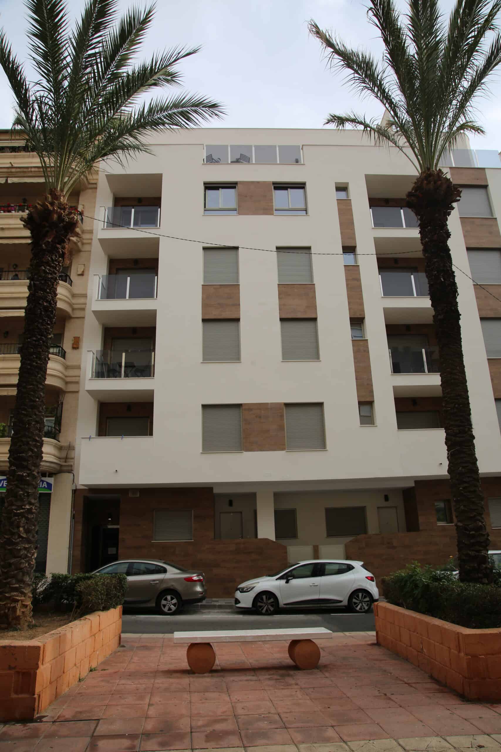 Appartementencomplex met moderne architectuur, palm bomen en parkeerplaatsen, gelegen aan Casa La Pluma, perfect voor comfortabel wonen in een architectonisch strak gebouw met natuurlijke omgeving.